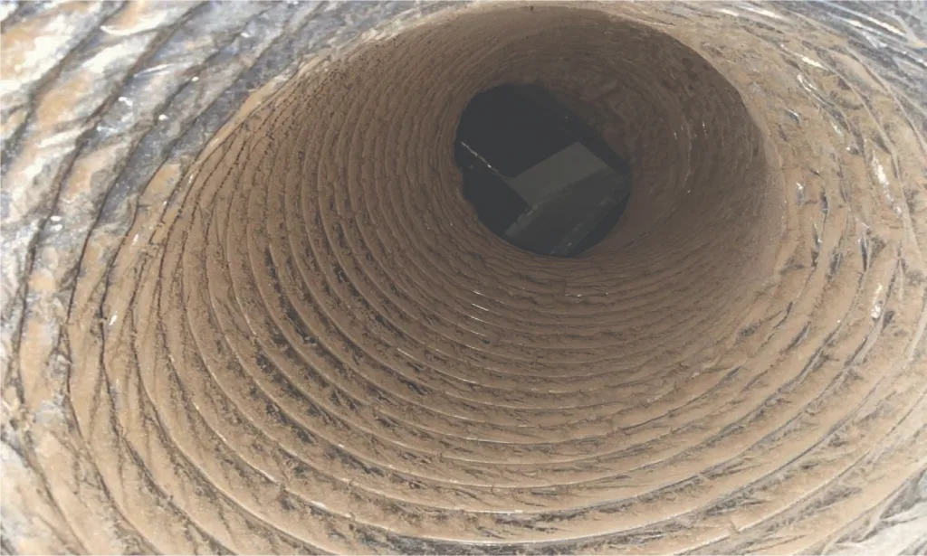Inside an air duct caked with dust before cleaning